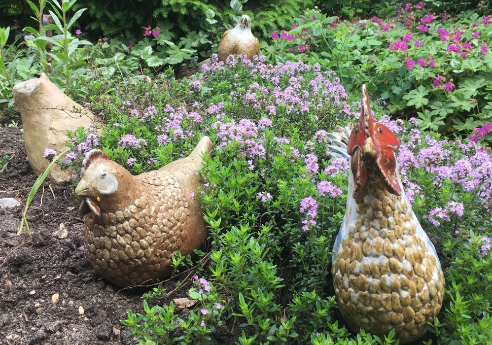 Getöpferte Hühner im Blumenbeet