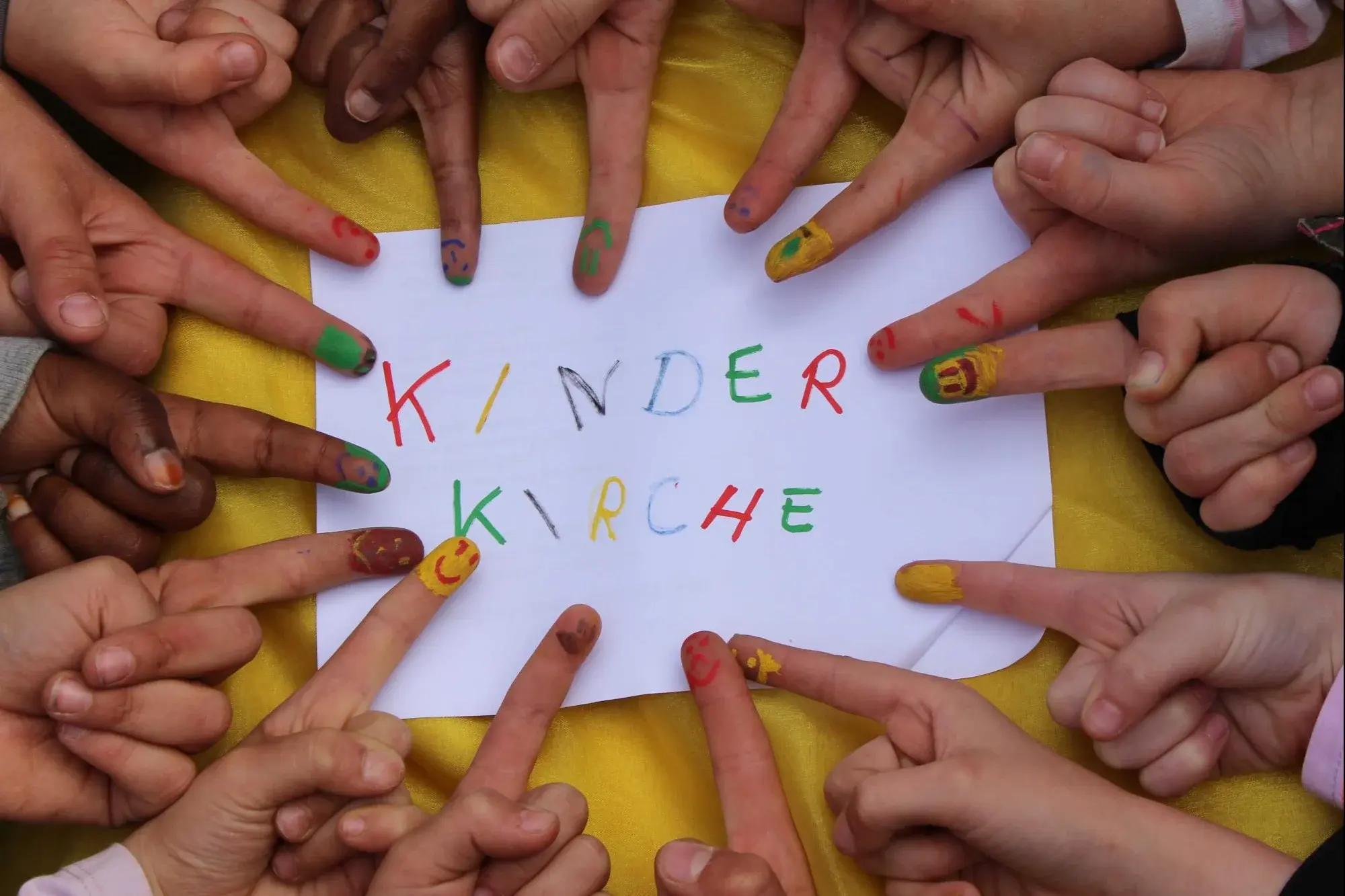 buntbemalte Kinderfinger zeigen auf das Schild Kinderkirche.